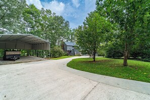 Une allée menant à une maison avec un garage fermé et un chemin bordé d’arbres.