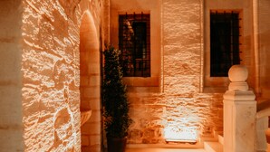 Un pasillo de paredes de piedra con una planta en maceta, una escalera y una ventana con barrotes.