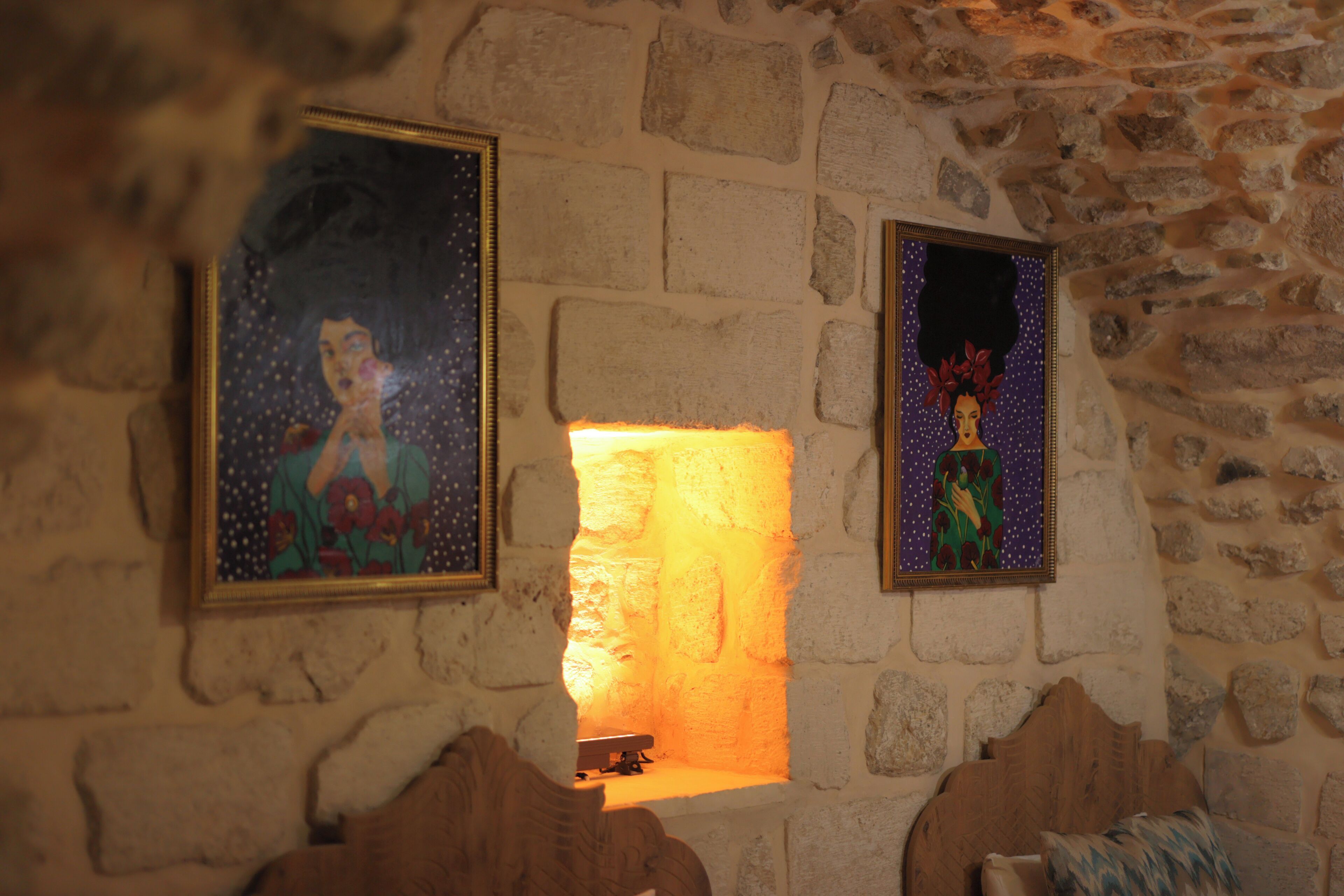 Paredes de pedra com duas pinturas emolduradas, lareira e um banco de madeira.