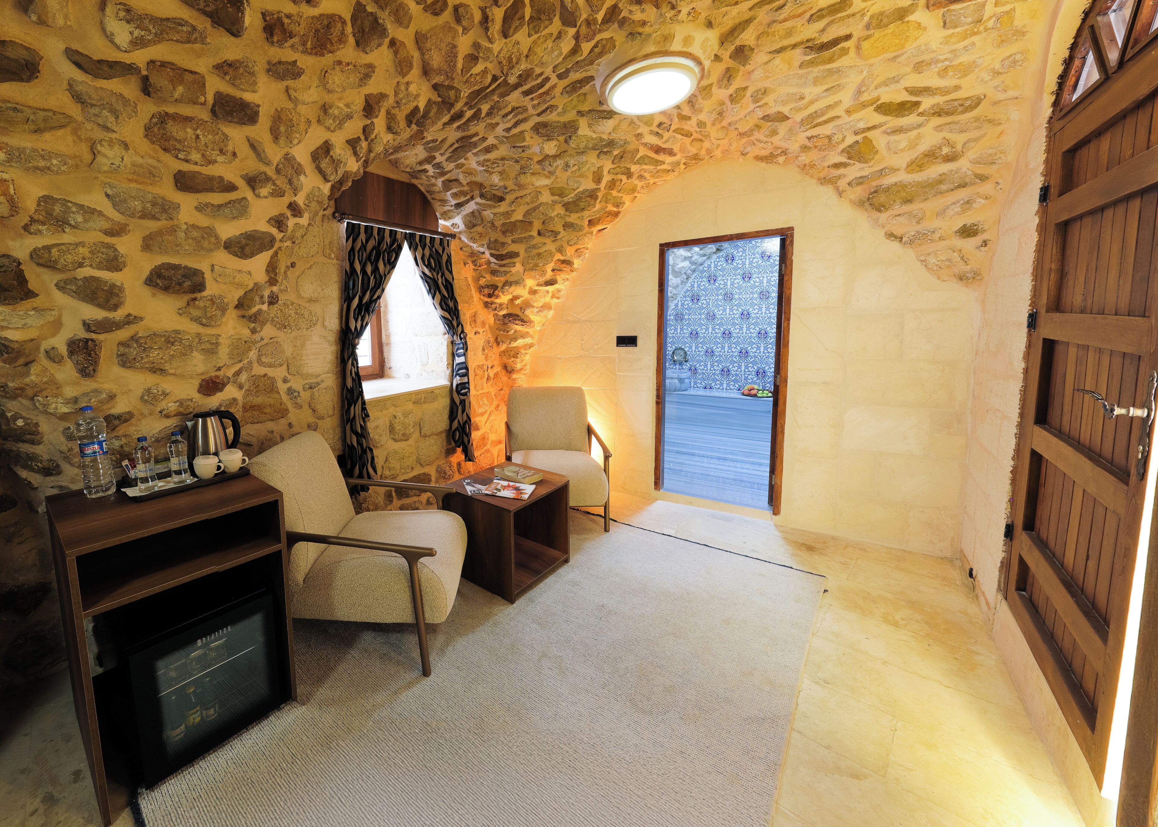 A cozy room with stone walls, a wooden door, a small table with a chair, and a radiator.