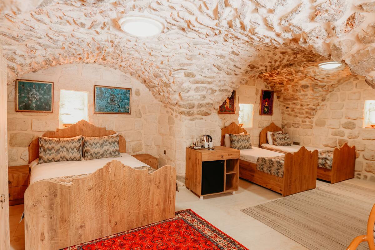Ein Zimmer mit Steinwänden und Holzboden, mit zwei Betten und passenden Kopfteilen sowie einem kleinen Holzschrank.