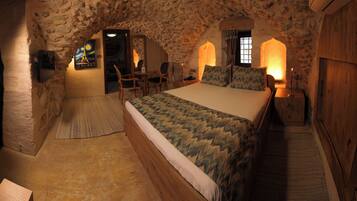 A rustic room with a stone ceiling, a wooden bed, a small table with chairs, and a painting on the wall.