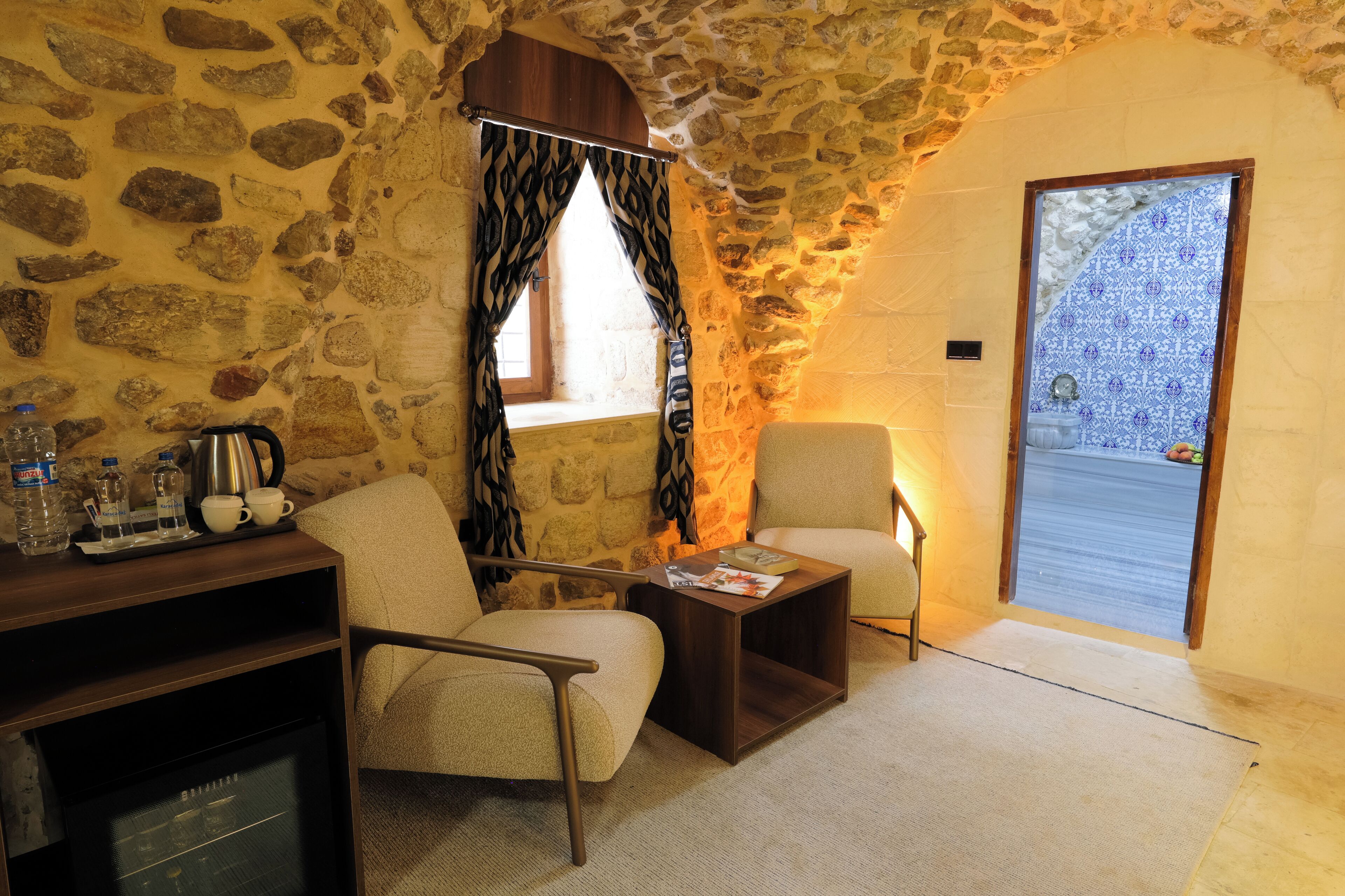 A cozy room with stone walls, a wooden cabinet, a sofa, a small table, and a view through a door with patterned tiles.
