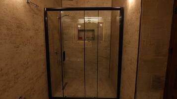 A glass-enclosed shower with a marble wall and a small shelf with toiletries.