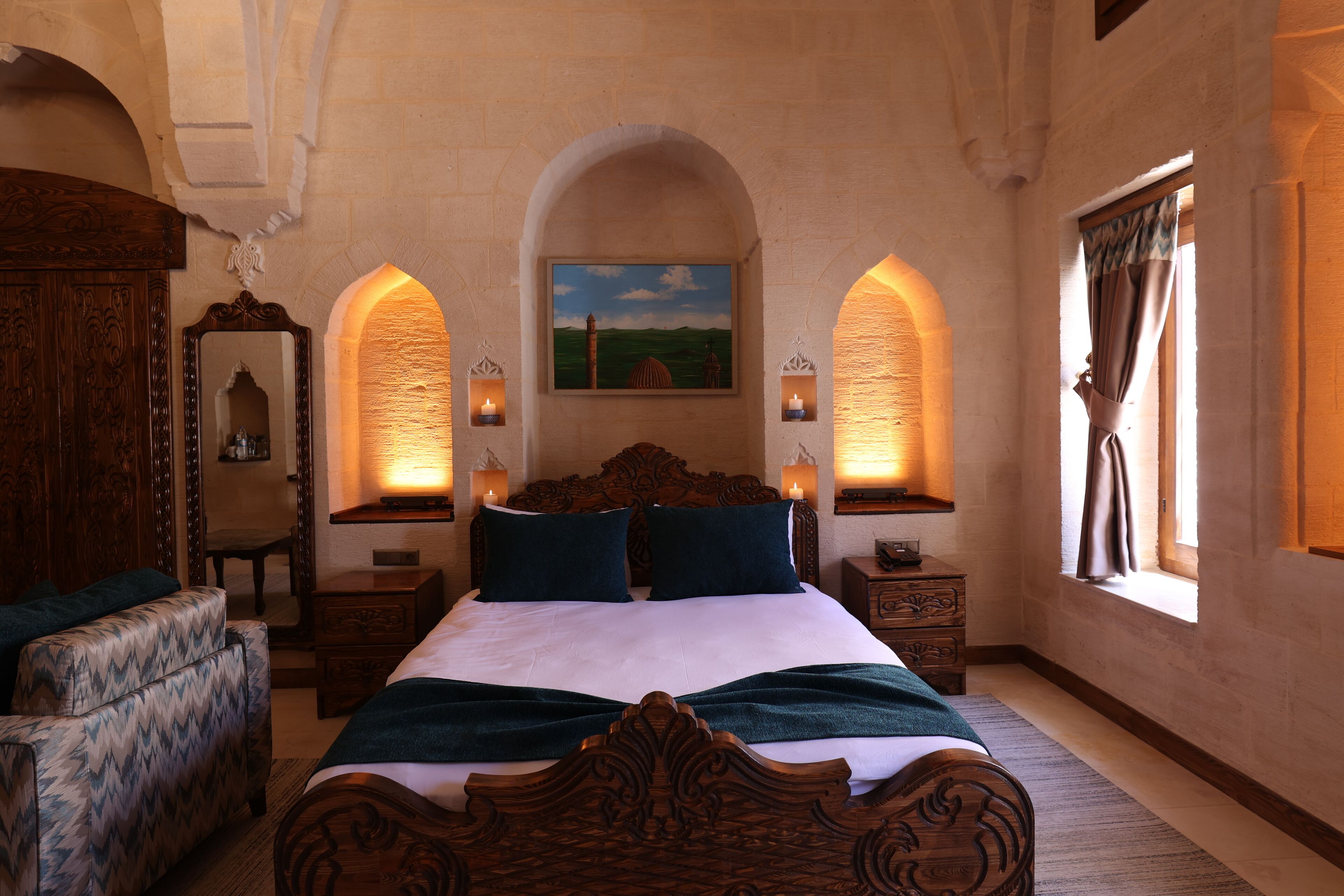 A bedroom with a large bed, two bedside tables, a wooden wardrobe, a chair, and a painting on the wall.