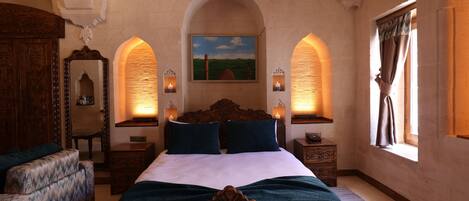 A bedroom with a large bed, two bedside tables, a wooden wardrobe, a chair, and a painting on the wall.