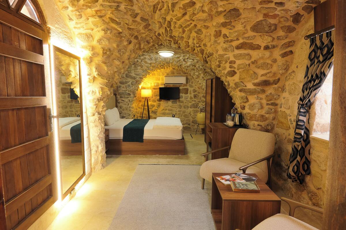Ein gemütliches Zimmer mit Steinwand, Holztür und einem Bett mit weißer Decke.