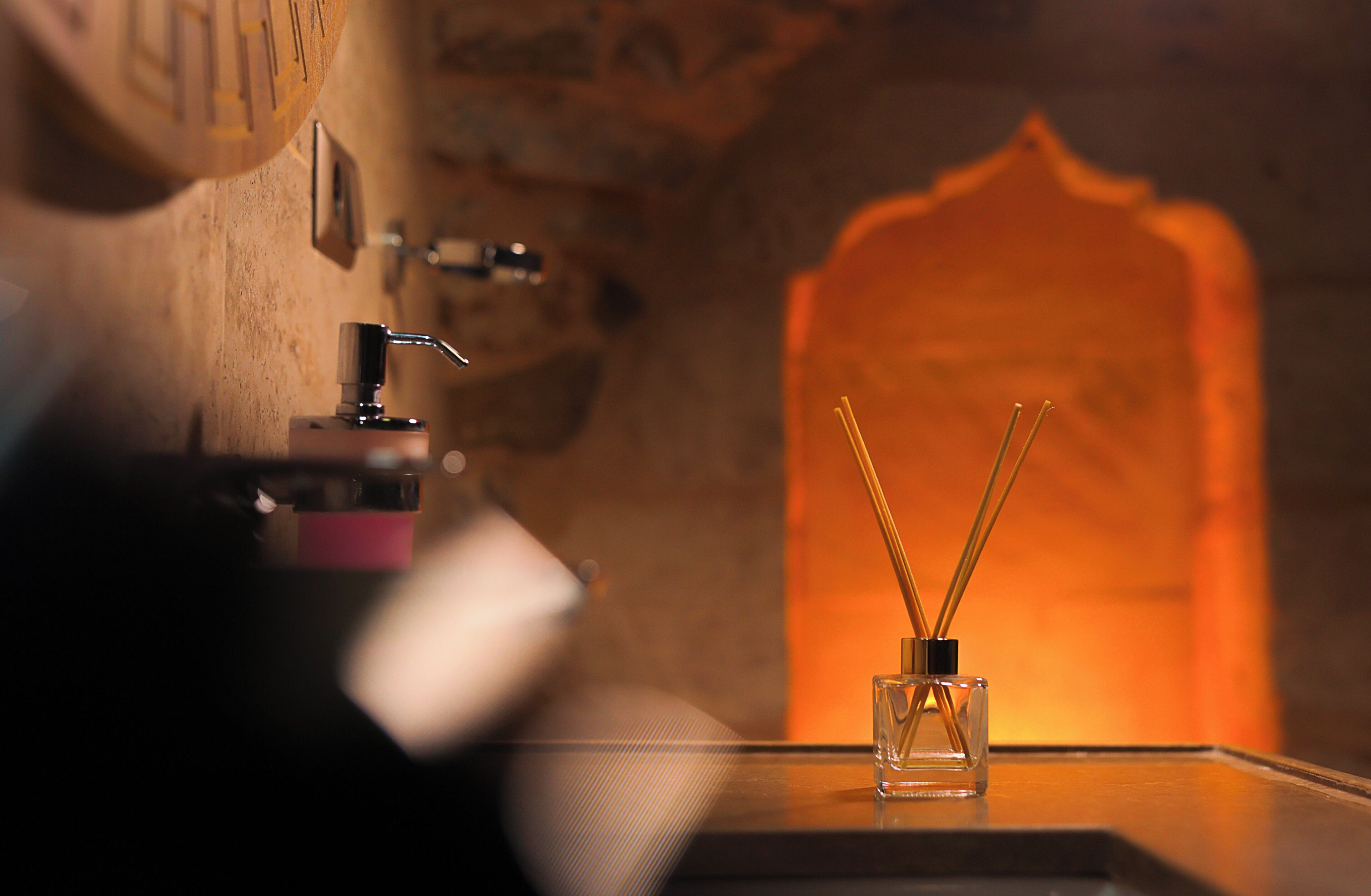 A bathroom with a sink, a mirror, and a glass container with reed diffusers.