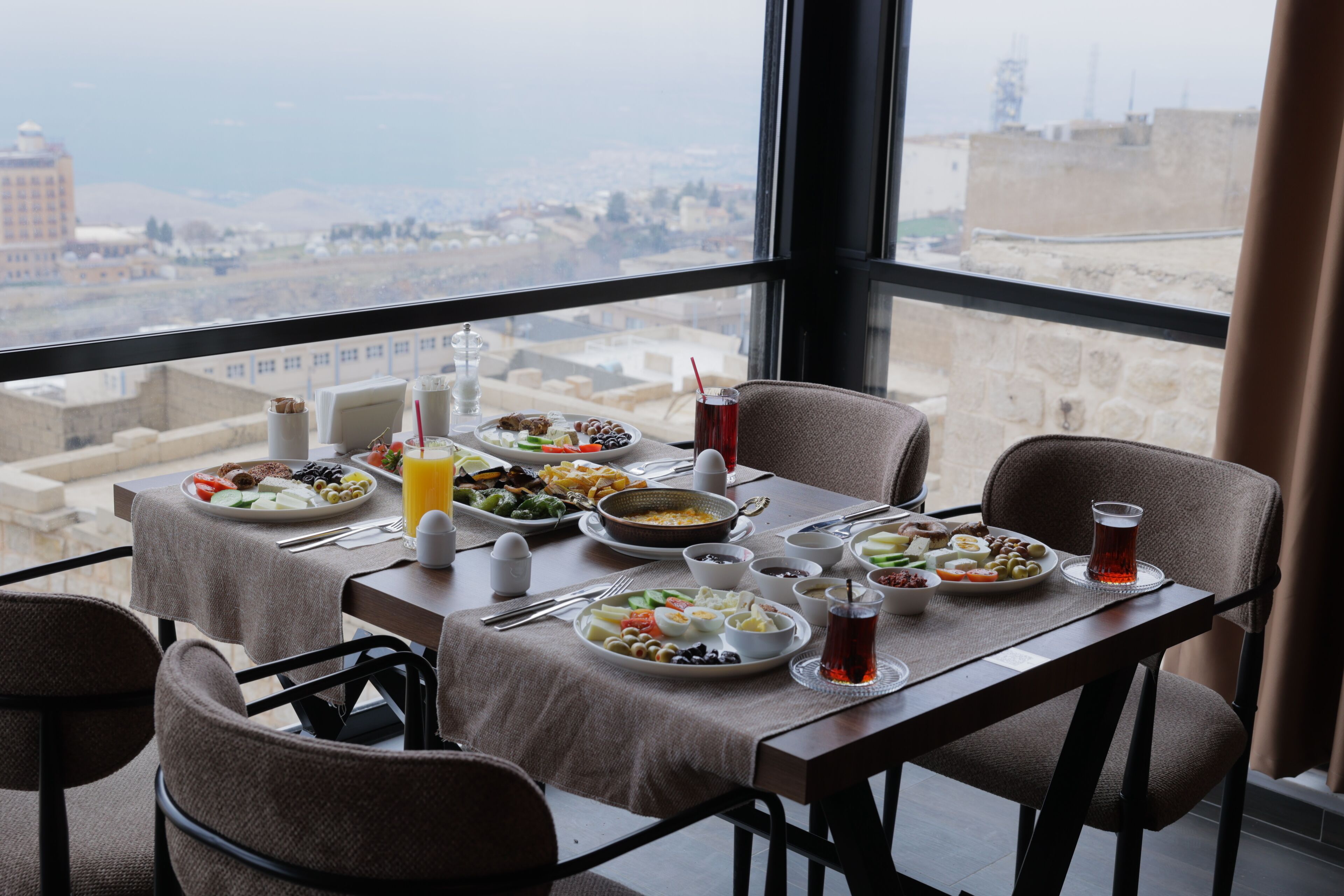 A dining table with various dishes and drinks, set against a city view.