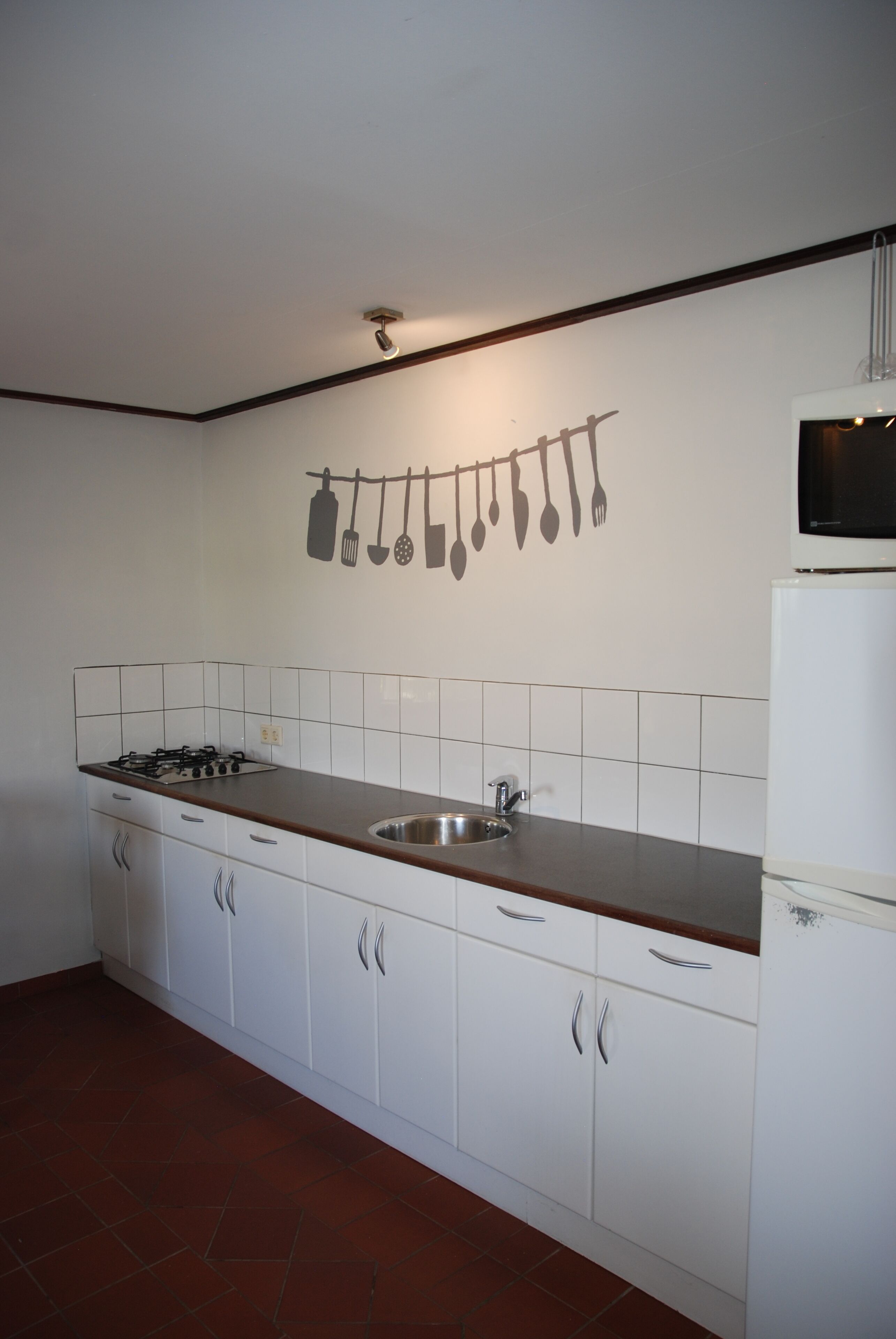 Una cocina con armarios blancos, encimera de madera, pileta de acero inoxidable y un colgador de utensilios en la pared.