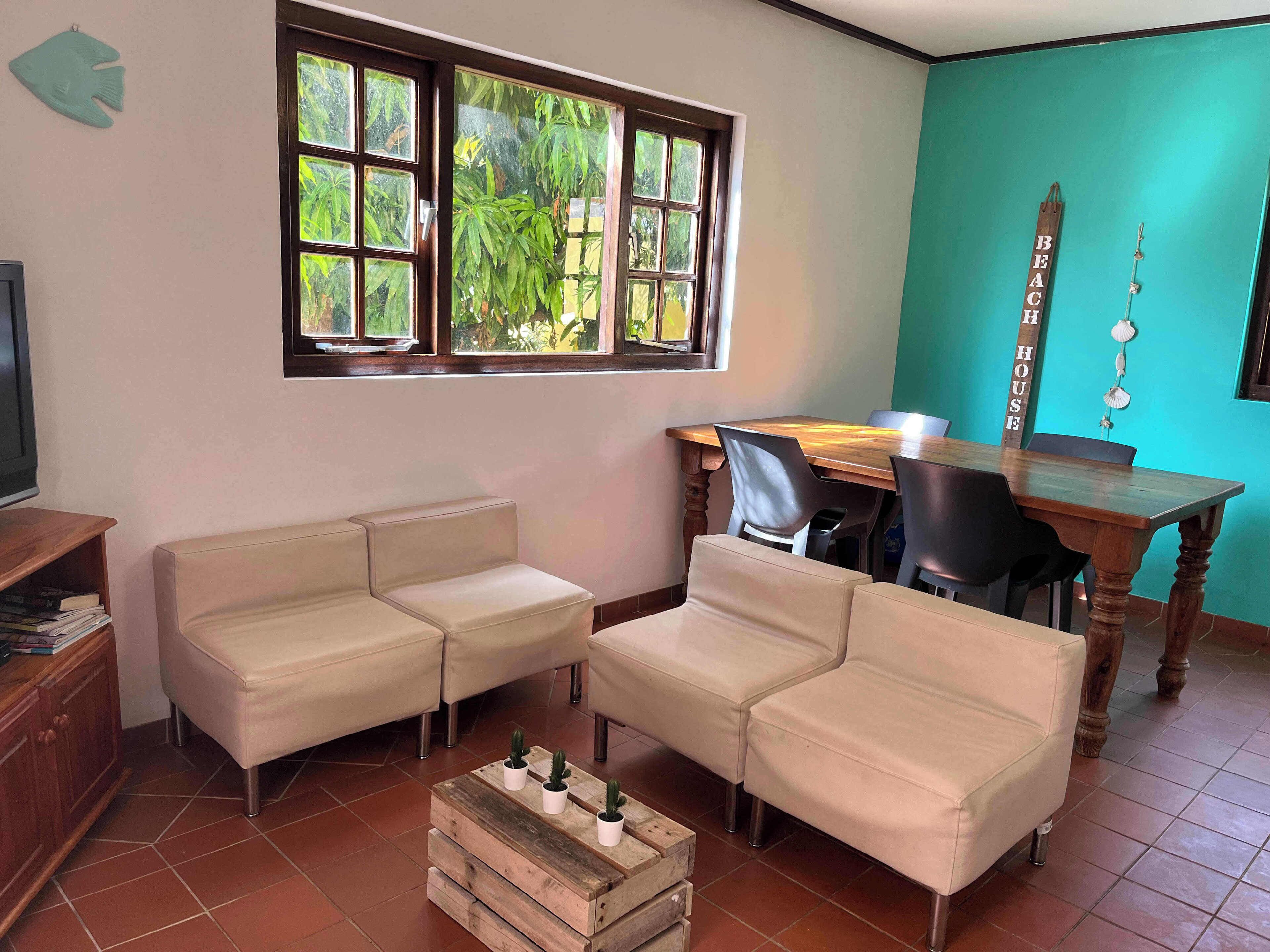 Un soggiorno con un tavolo da pranzo in legno, due divani color beige, un tavolino da caffè con dei cactus, una TV su un mobiletto in legno e una finestra vista verde.