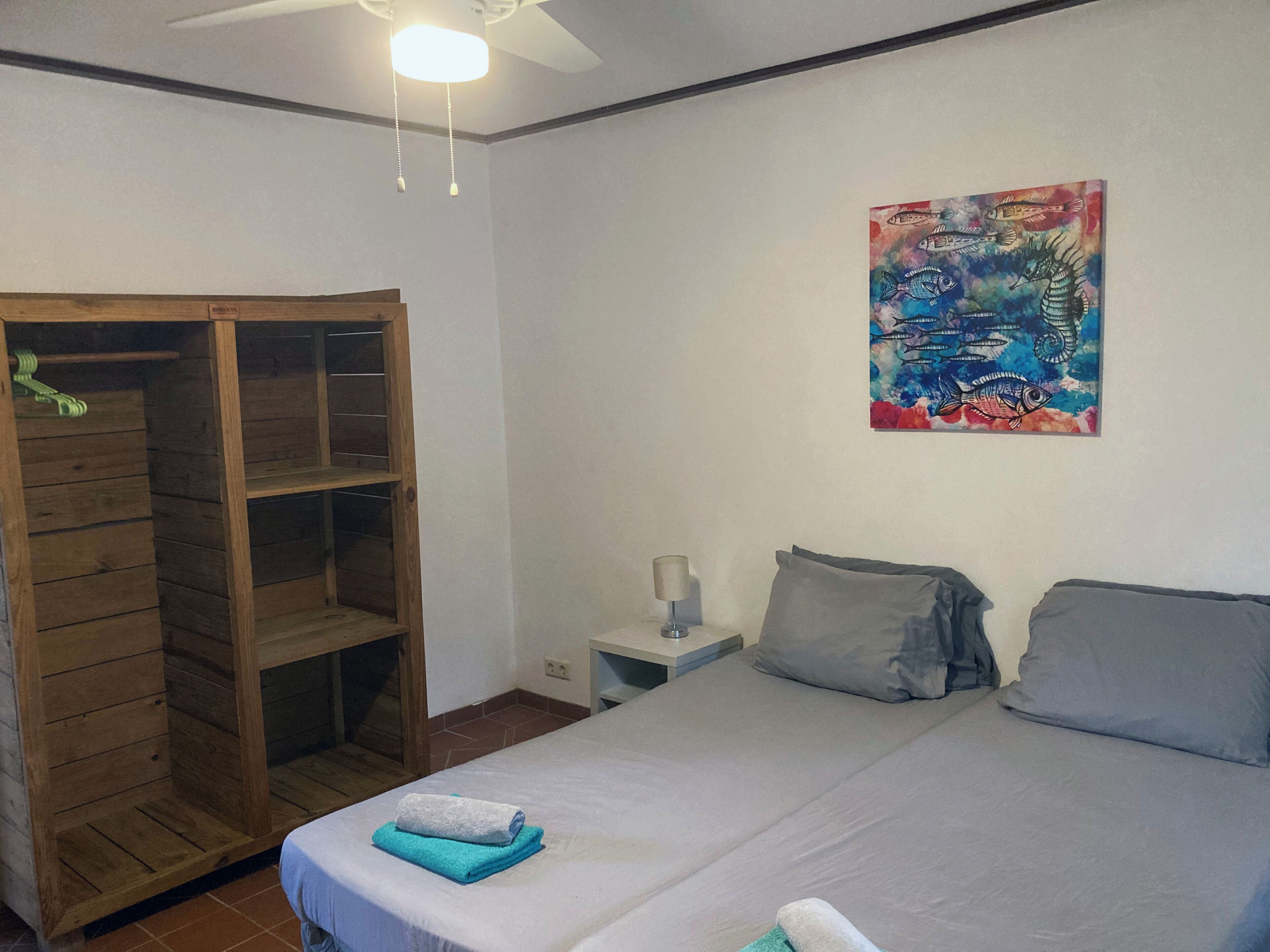 A bedroom with a bed, a wooden wardrobe, a nightstand, and a colorful fish painting on the wall.