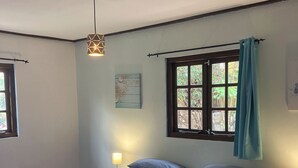 A bedroom with a large bed, two bedside tables, a hanging light fixture, a window with curtains, and a wall-mounted artwork. - Mirador Apartments (Willemstad)