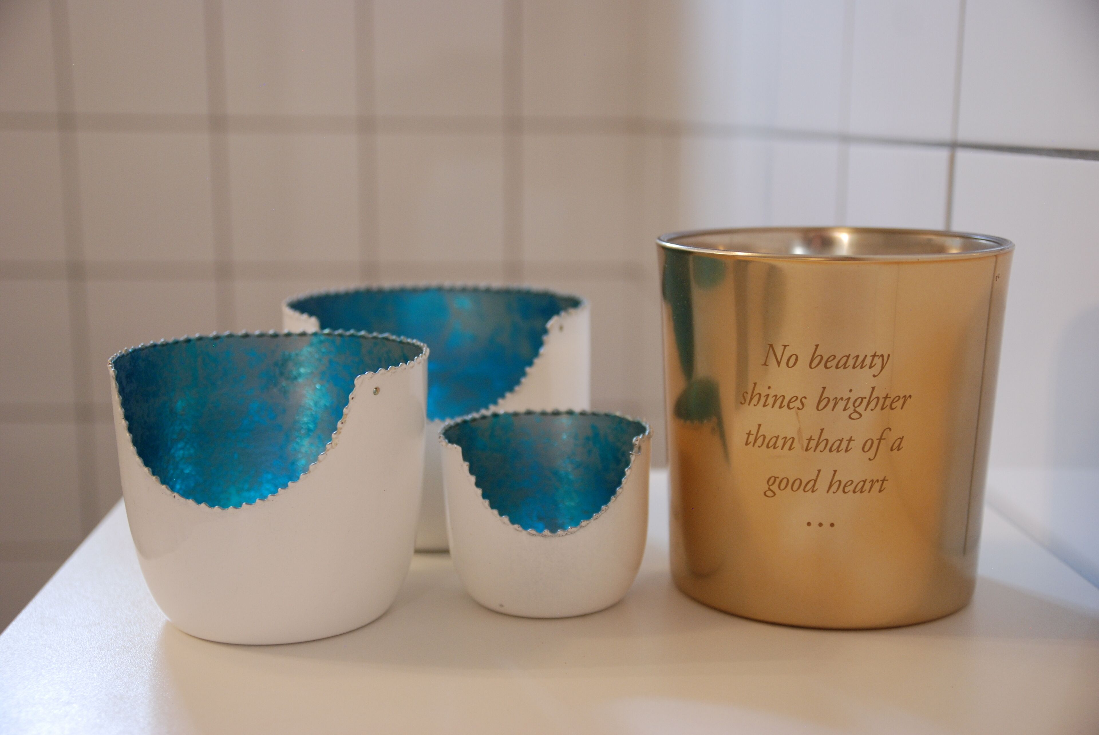 Drei Kerbecher mit blauen Akzenten und eine goldene Tasse mit einem Zitat.