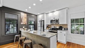Una cocina moderna con armarios blancos, una isla central con taburetes, un refrigerador, un microondas y una estufa.
