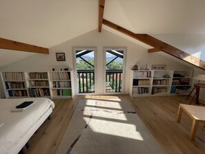 Ein geräumiges Schlafzimmer im Dachgeschoss mit einem großen Oberlicht, Holzbalken und einem Balkon mit Blick ins Freie.