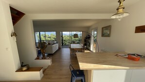 Eine geräumige Küche mit einer Holztischinsel, einem Essbereich mit Tisch und Stühlen sowie Blick ins Freie durch große Fenster.