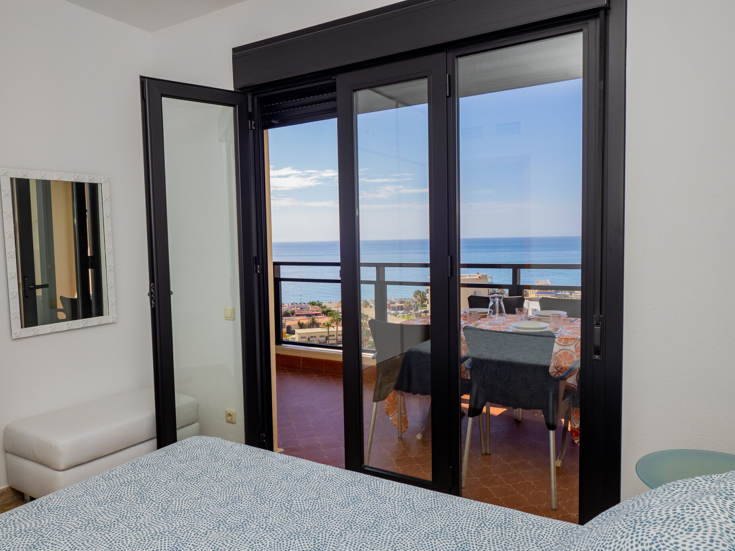 Ein Zimmer mit einem Bett, einer Bank und einer Schiebetür, die auf einen Balkon mit Tisch und Stühlen führt.