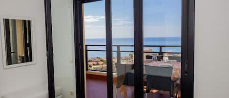 Una habitación con una cama, un banco y un ventanal corredero que da a un balcón con una mesa y sillas.