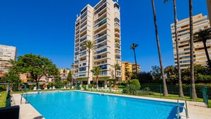Una piscina circondata da alti edifici residenziali, palme e un cielo azzurro limpido.