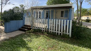 A small, single-story house with a white picket fence, a wooden deck, and a small porch. - Mobil Home/bungalow 6 Places Camping 4 (Hyères)