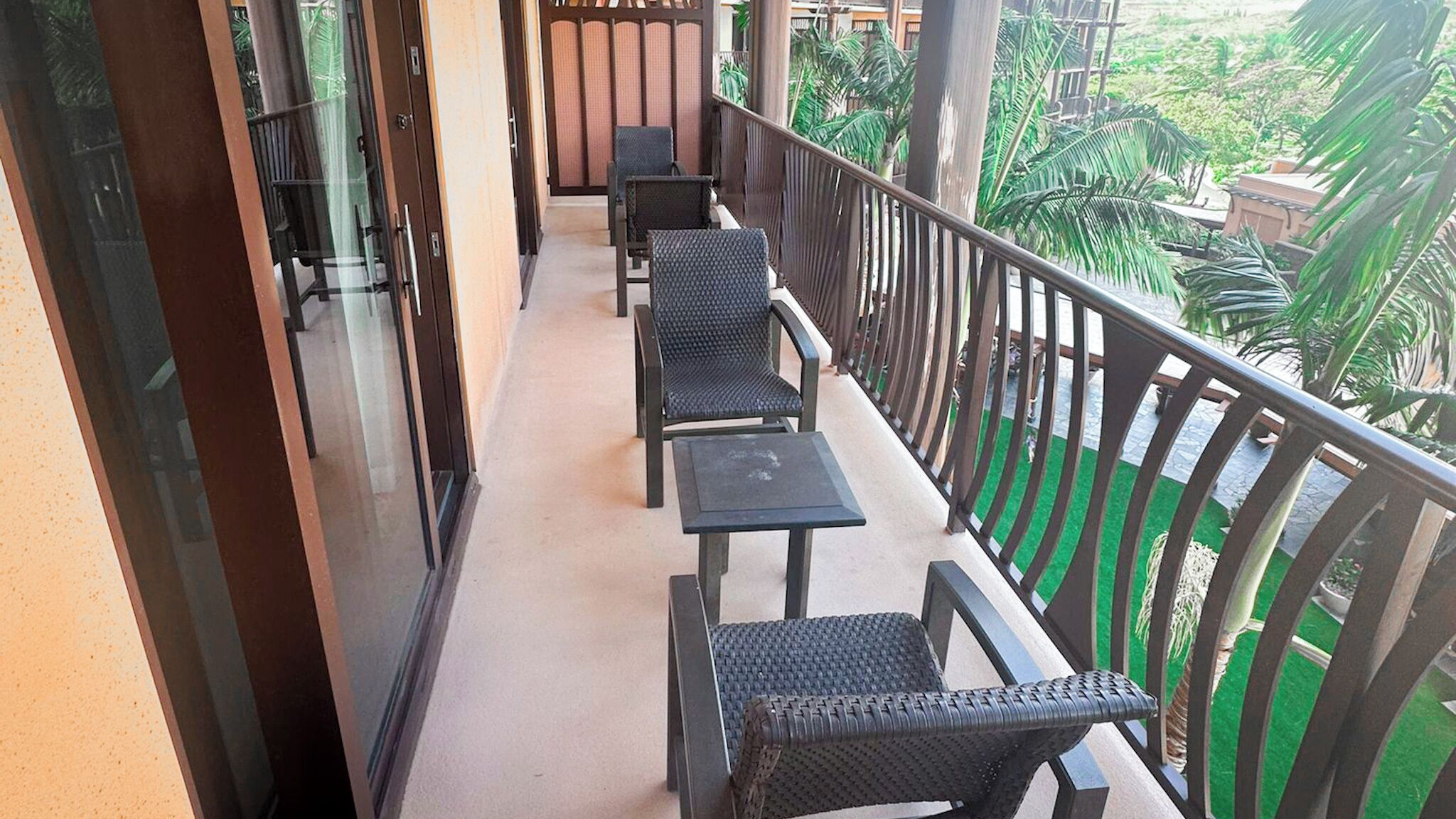 A balcony with a row of chairs and tables, a glass door, and a view of greenery.
