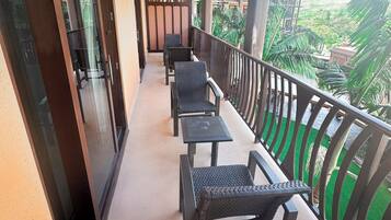 A balcony with a row of chairs and tables, a glass door, and a view of greenery.