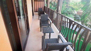 A balcony with a row of chairs and tables, a glass door, and a view of greenery.