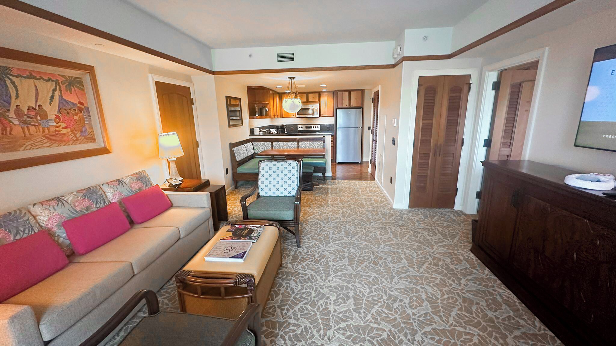 Una habitación de hotel con sofá, mesa de comedor, zona de cocina y televisor.