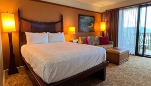 A hotel room with a large bed, two bedside lamps, a sofa with cushions, a small table, and a painting on the wall.