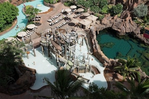 Vue aérienne d’un complexe hôtelier doté d’une piscine centrale, de nombreuses chaises longues et d’un paysage rocheux.