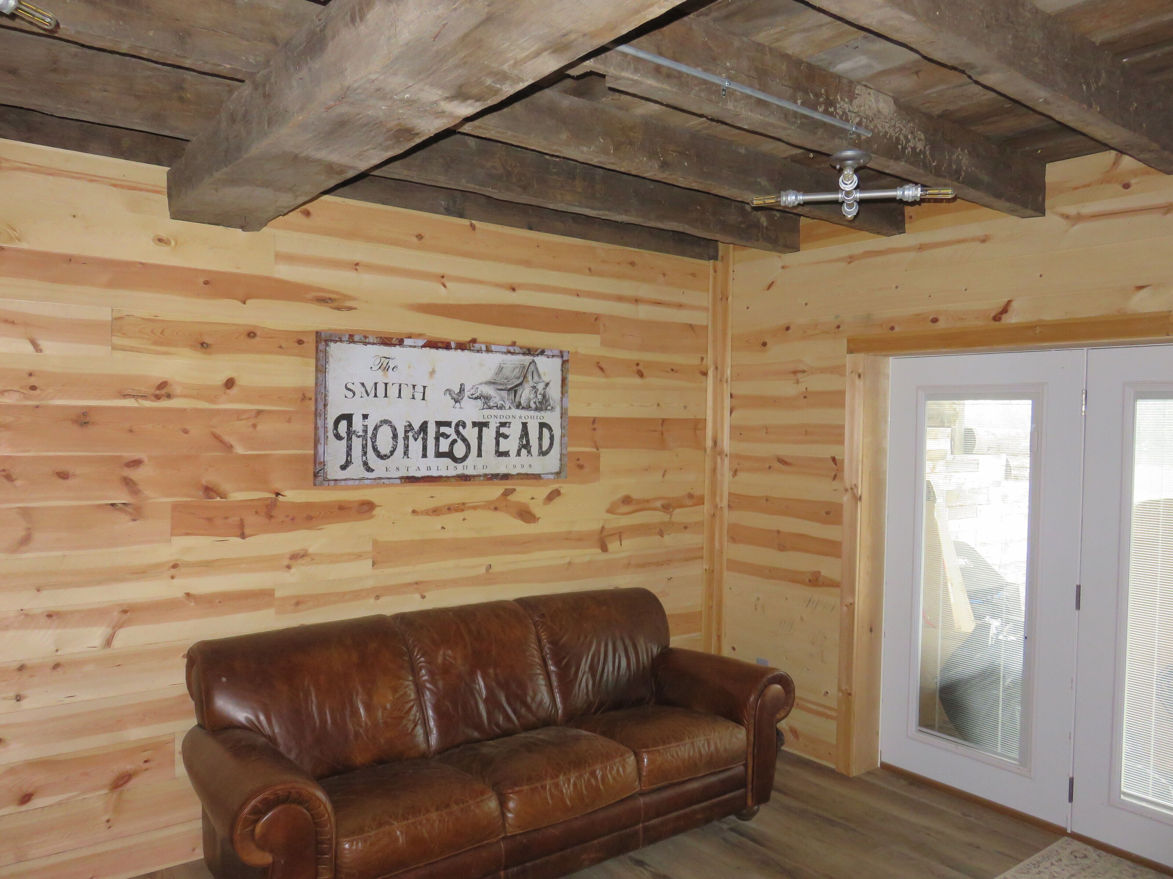Una habitación con paredes de madera, un sofá de cuero marrón, un ventilador de techo y un letrero que dice "The Smith Homestead Established 1995".