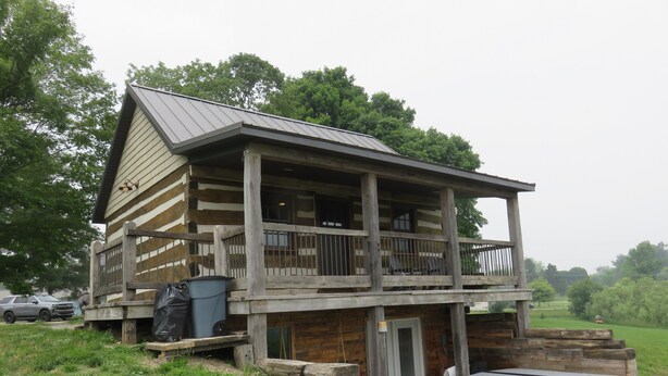 A log cabin with a balcony, a hot tub, and a stone wall.