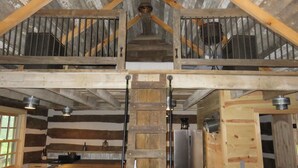 A rustic cabin interior with a loft bedroom, a kitchen area, and a dining space.