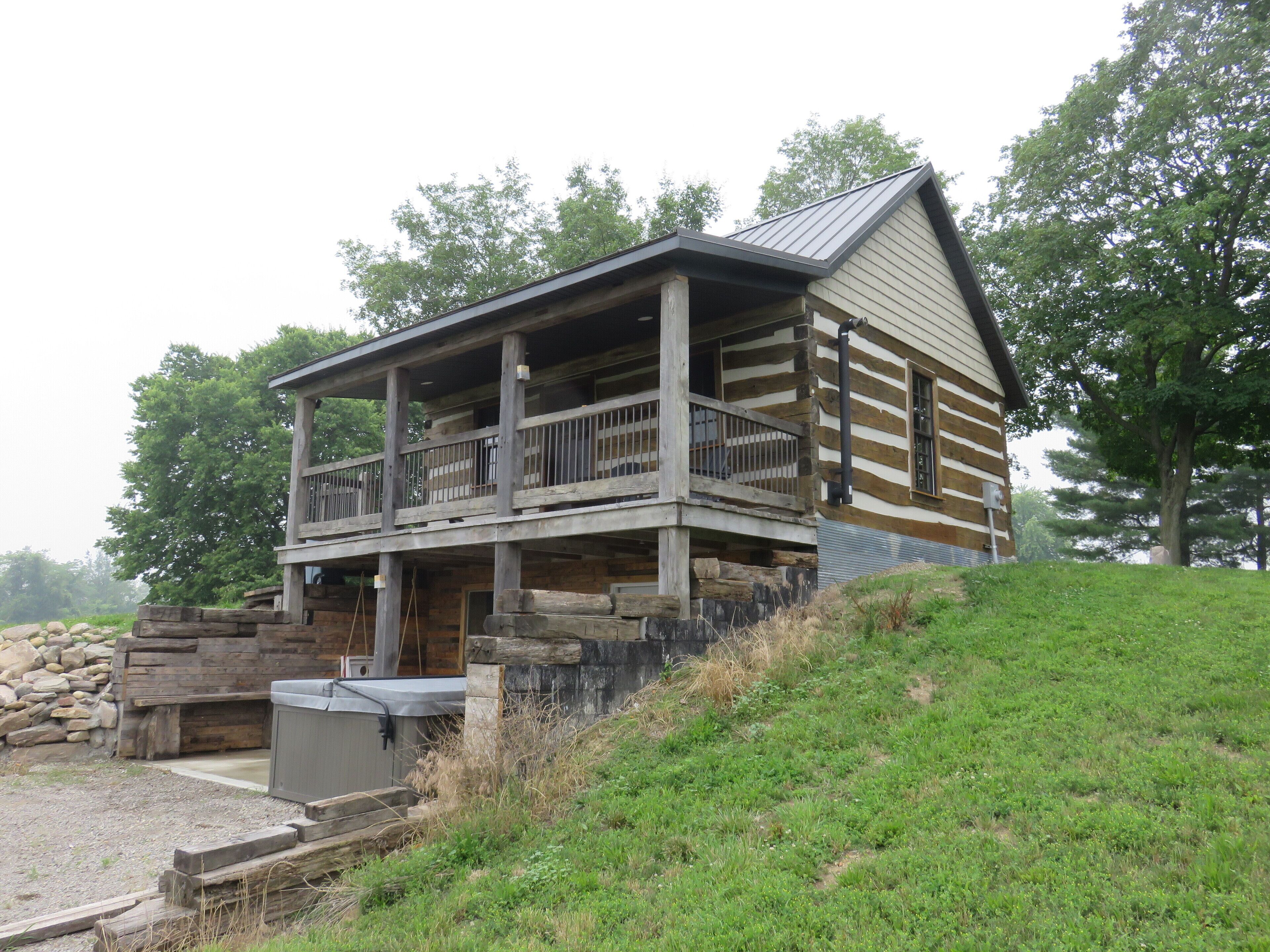 A log cabin with a balcony, a hot tub, and a stone wall.