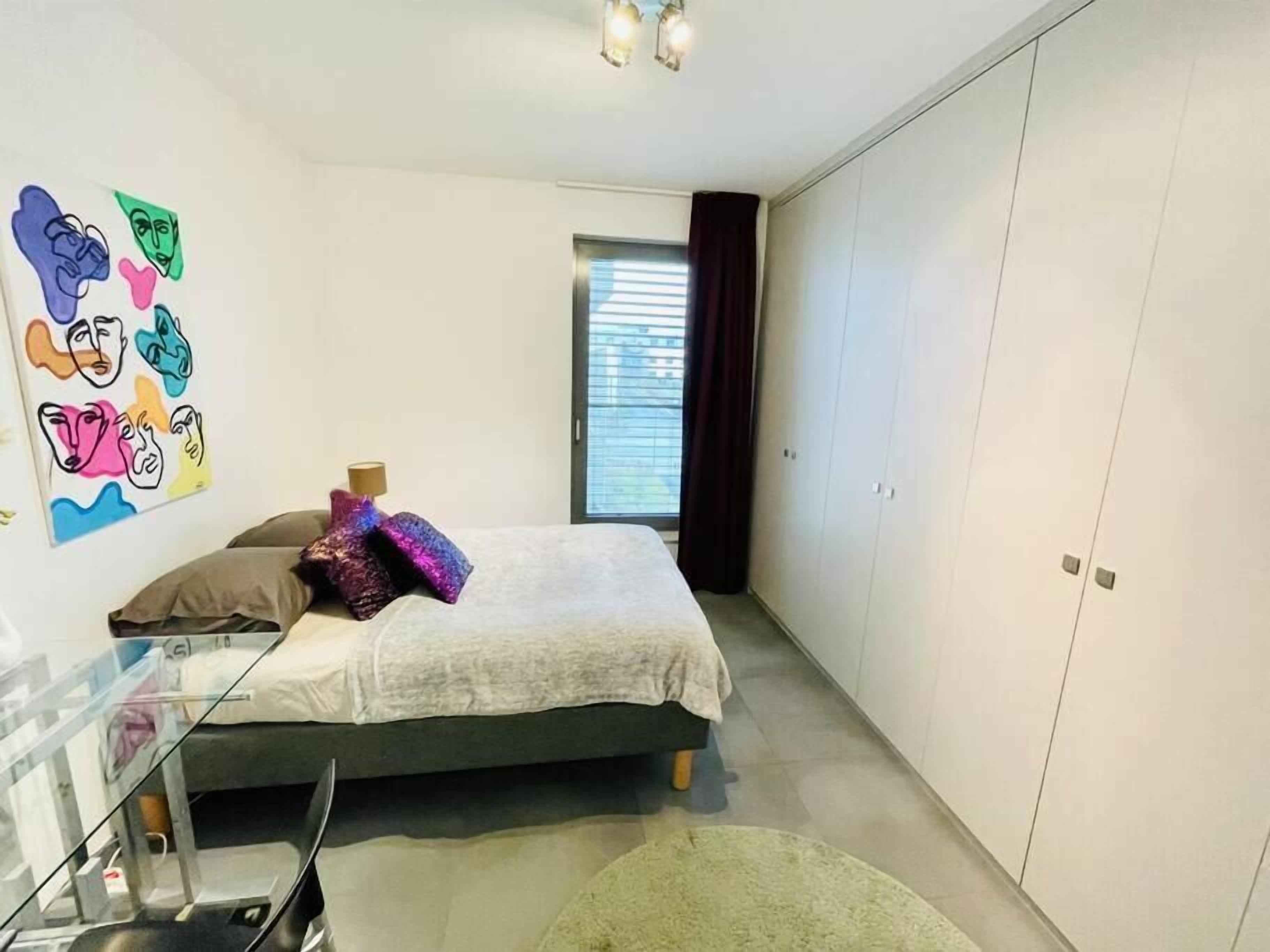 A bedroom with a bed, a desk, a wardrobe, and a window with curtains.