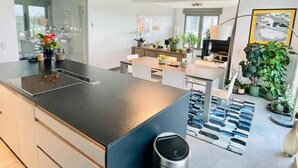 A modern kitchen with a central island, a dining area with a table and chairs, and a living space with a sofa and a TV. - Luxury 3 bedrooms- Terrace and Parking (Bertrange)
