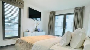 A hotel room with a bed, a TV mounted on the wall, a dresser, and a window with curtains. - Luxury 3 bedrooms- Terrace and Parking (Bertrange)