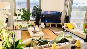A modern living room with a large flat-screen TV, comfortable seating, and large windows offering a view of the cityscape. - Luxury 3 bedrooms- Terrace and Parking (Bertrange)