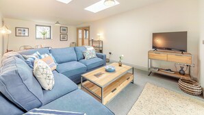 Ein Wohnzimmer mit einem Ecksofa, einem Flachbildfernseher, einem Couchtisch und einem Fenster mit Tageslicht.