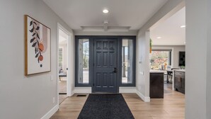A modern home interior with a dark wooden door, a black doormat, and a kitchen area visible through an open door.