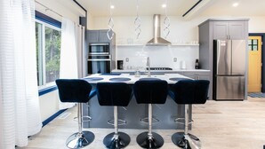 A modern kitchen with a central island, bar stools, stainless steel appliances, and a view of the outdoors. - Notre Dame Home Steps to Campus w/ Hot Tub (South Bend)