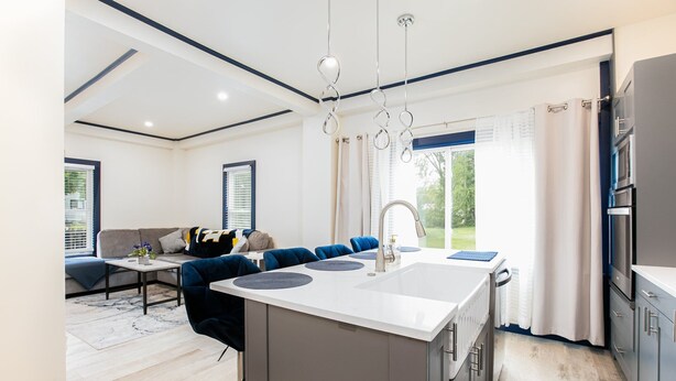 A modern kitchen with a central island, a dining area with blue chairs, and a living room with a sofa and a coffee table. - Notre Dame Home Steps to Campus w/ Hot Tub (South Bend)