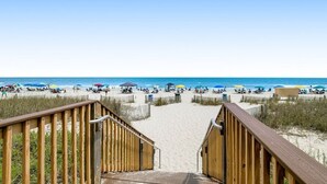 A wooden staircase leading to a sandy beach with umbrellas and beachgoers.