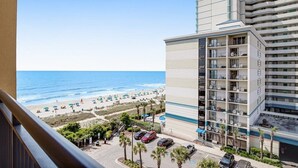 A hotel with a view of the beach, multiple balconies, and a parking area.