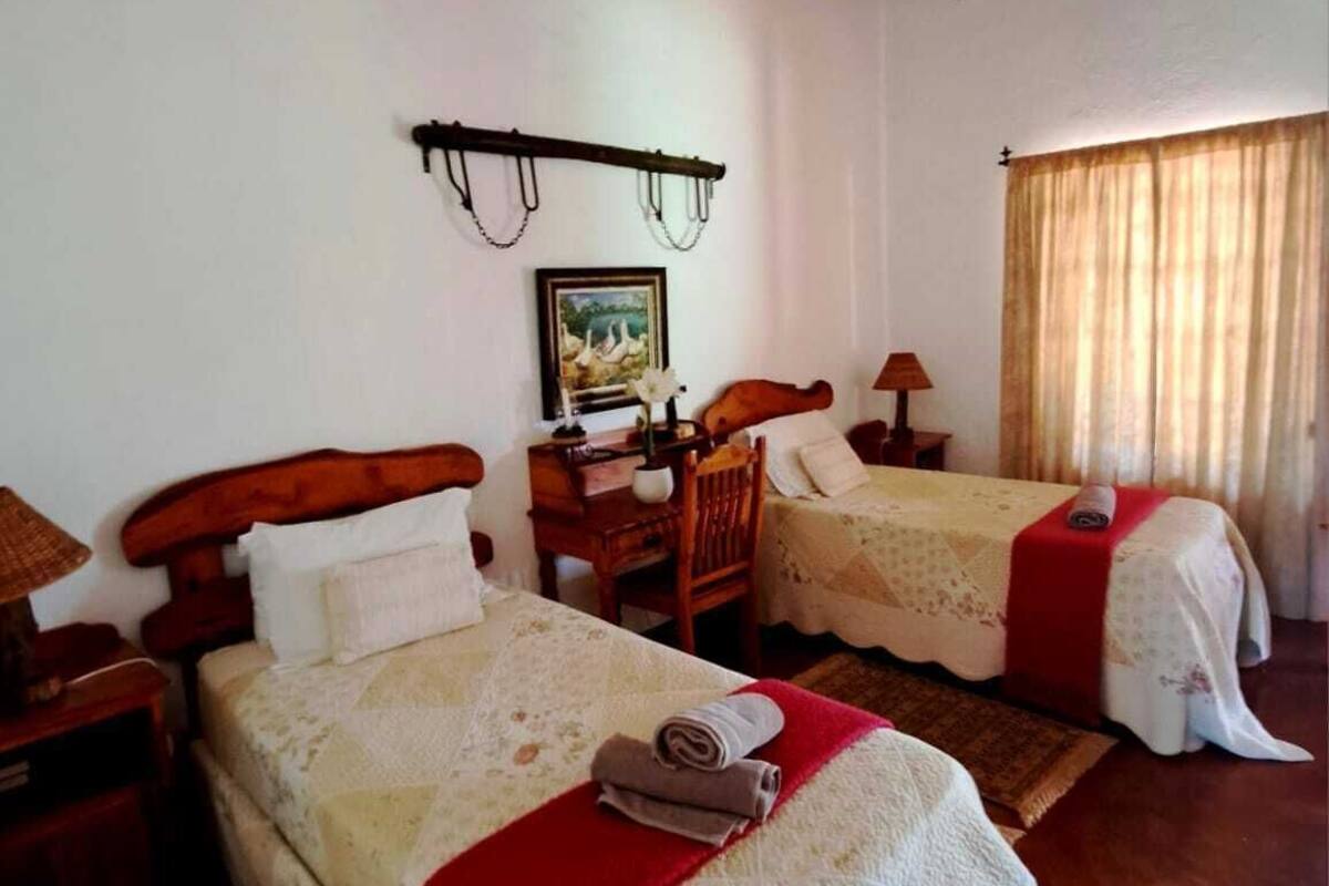 A room with two beds, each with a wooden headboard, a small table with a lamp, and a picture on the wall.