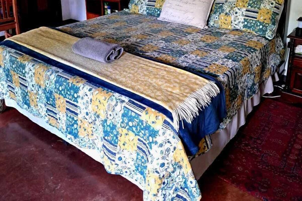 A bedroom with a large bed, a wooden headboard, a nightstand, a mirror, and a patterned bedspread.