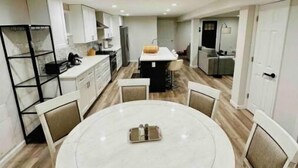 Uma cozinha moderna com armários brancos, uma ilha central e um espaço de refeições com mesa redonda e cadeiras.