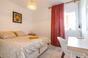 A bedroom with a bed, bedside table, lamp, and a view of the outdoors.