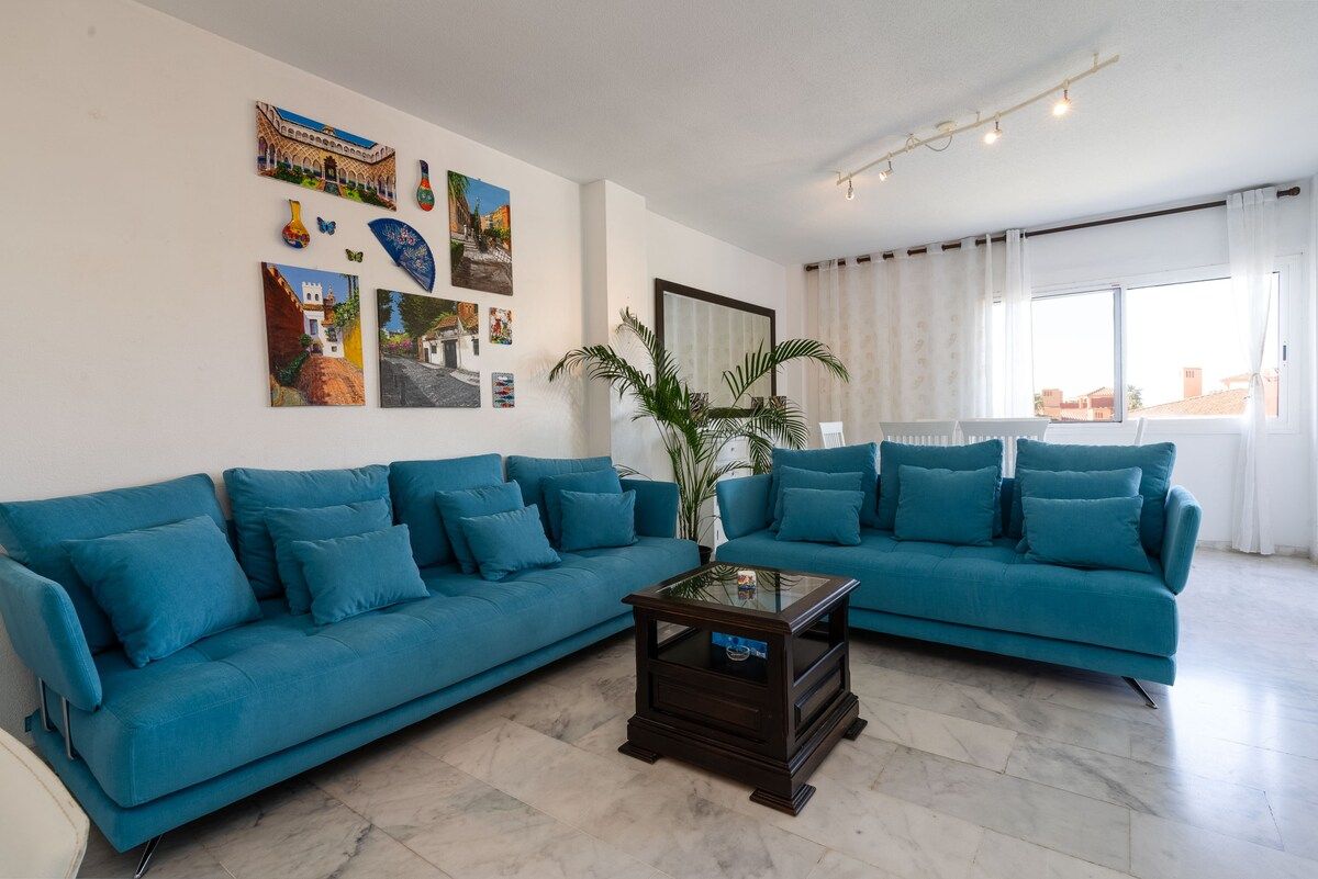A living room with two blue sofas, a coffee table, and wall art.